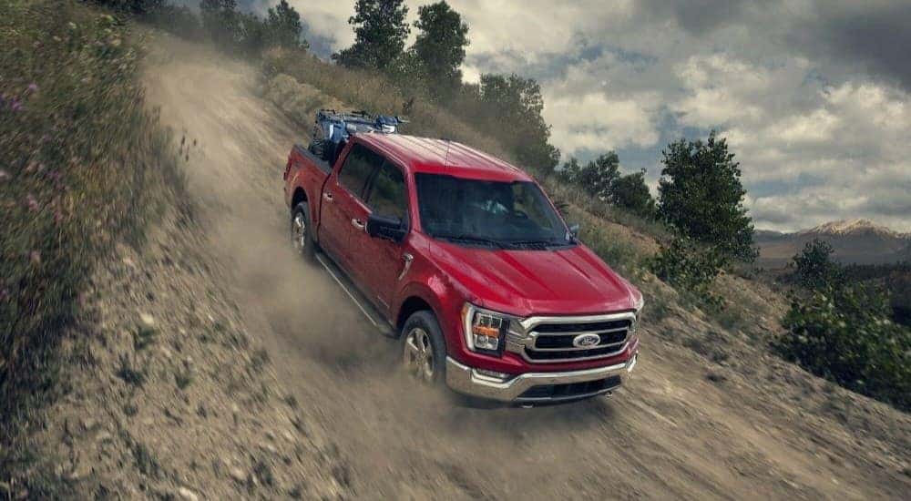 Red 2023 Ford F-150 driving off-road down a steep hill.