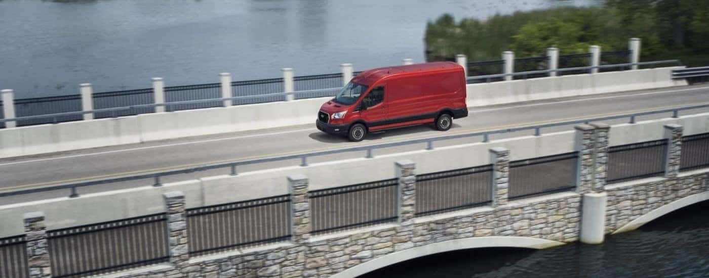 A red 2023 Ford Transit van is shown driving on a bridge.