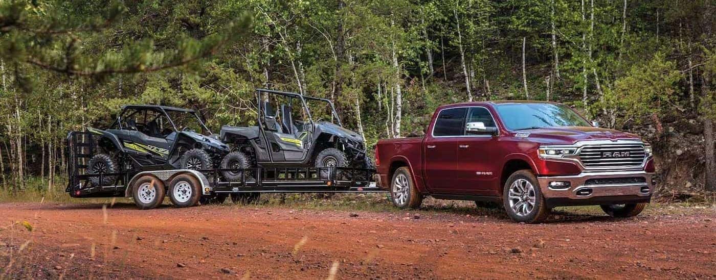 A red 2023 Ram 1500 is shown parked off-road while towing a trailer.