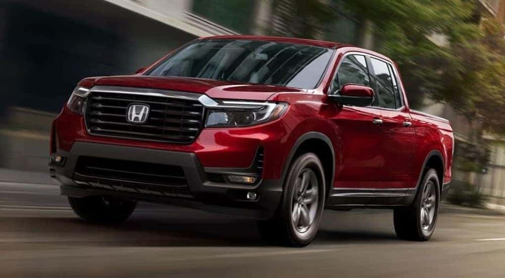 Red 2023 Honda Ridgeline RTL-E driving through a city after viewing a used trucks for sale near Troy.
