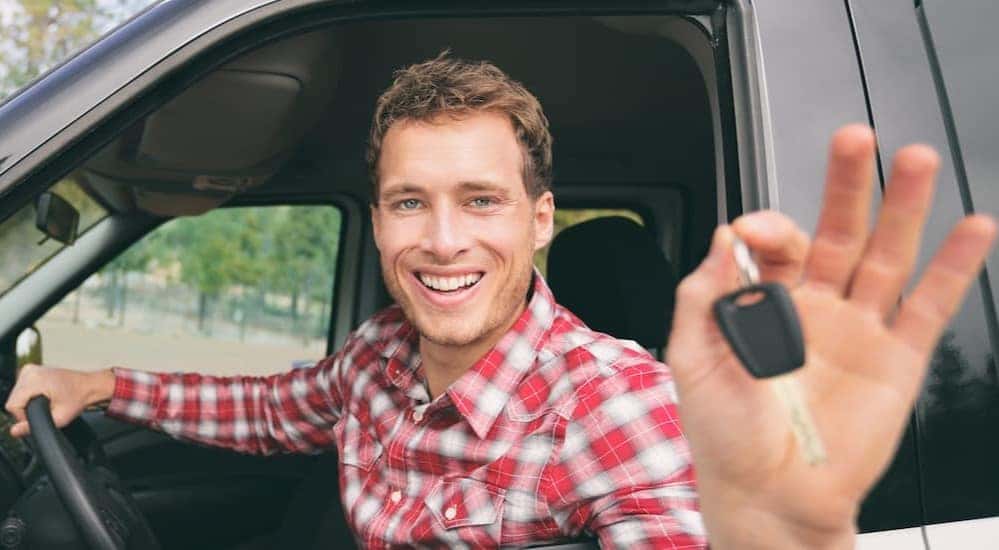 A person is shown holding keys after viewing used trucks for sale near Troy.
