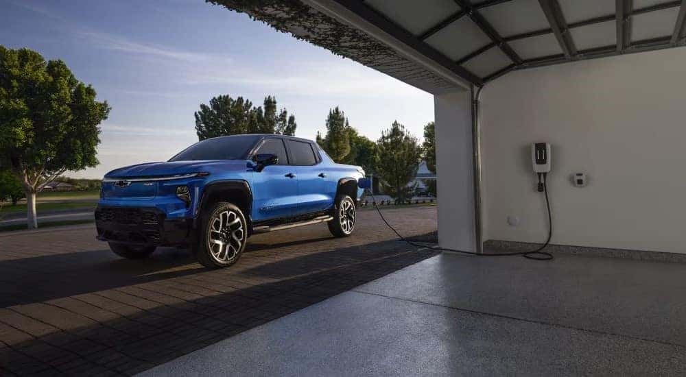 A blue 2024 Chevy Silverado EV RST parked near an open garage and charging.