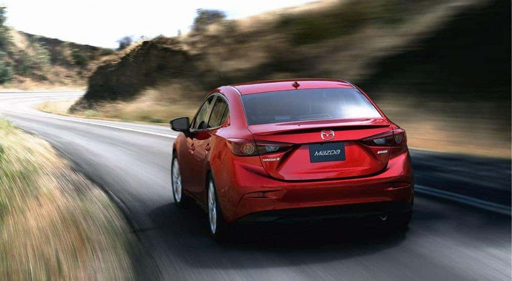 Red 2014 Mazda3 driving down a winding road.