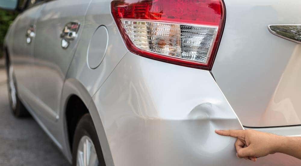 A person is shown pointing out a dent on a car.