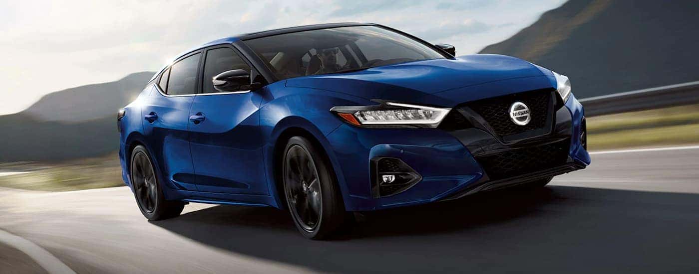 A blue 2021 Nissan Maxima is shown driving on a sunny day.