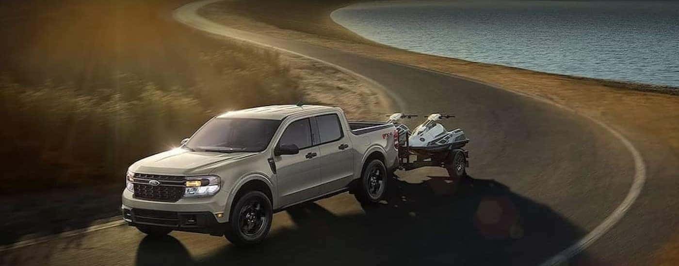 A silver 2024 Ford Maverick FX4 is shown towing a trailer near a lake.