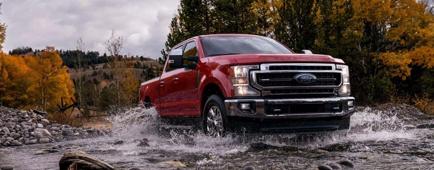 A red 2021 Ford F-250 driving over a shallow river.