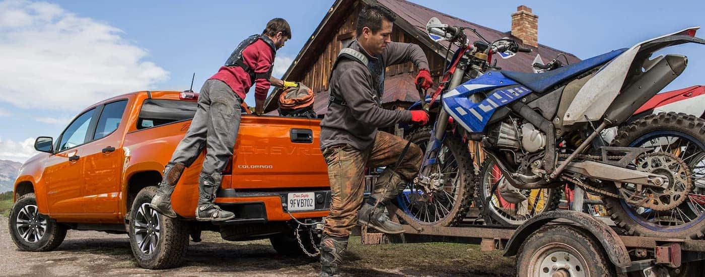 Group of people next to an orange 2022 Chevy Colorado hooked up to a trailer.