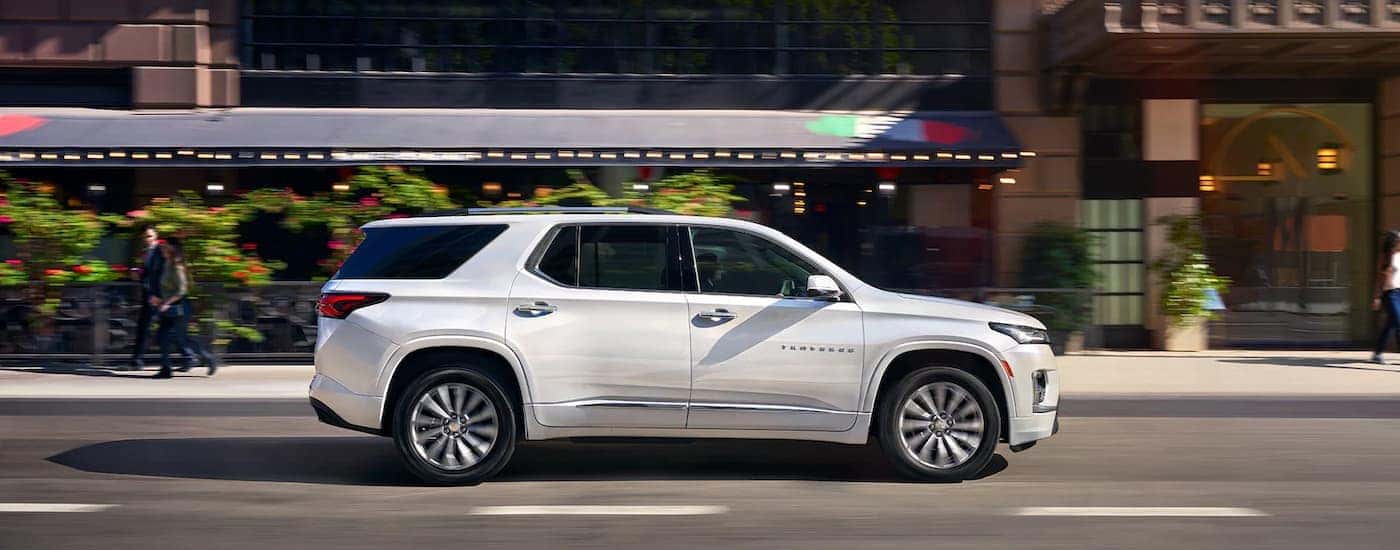 White 2023 Chevy Traverse driving on city street.