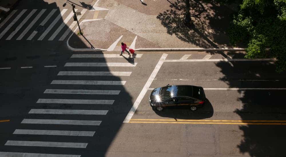 Car stopped at a crosswalk near a used car dealership