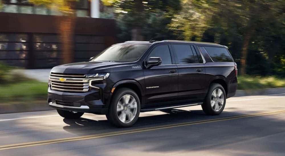 A blue 2024 Chevy Suburban High Country driving near a house.