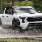 A white 2024 Toyota Tacoma driving through water.
