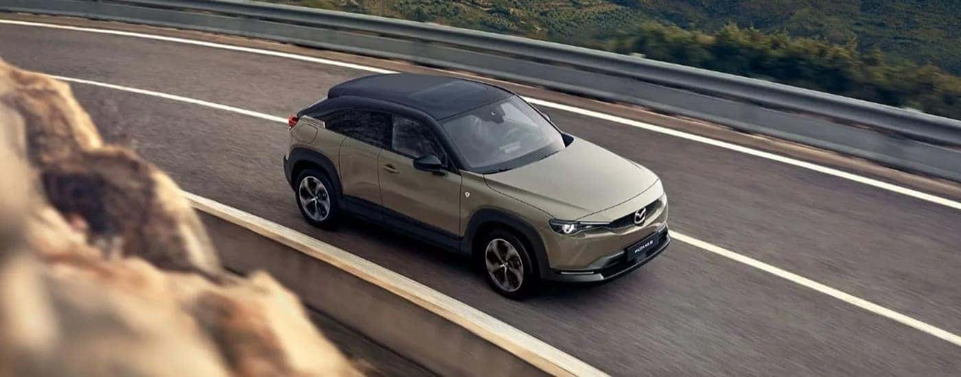 A tan 2024 Mazda MX-30 driving on a winding highway.