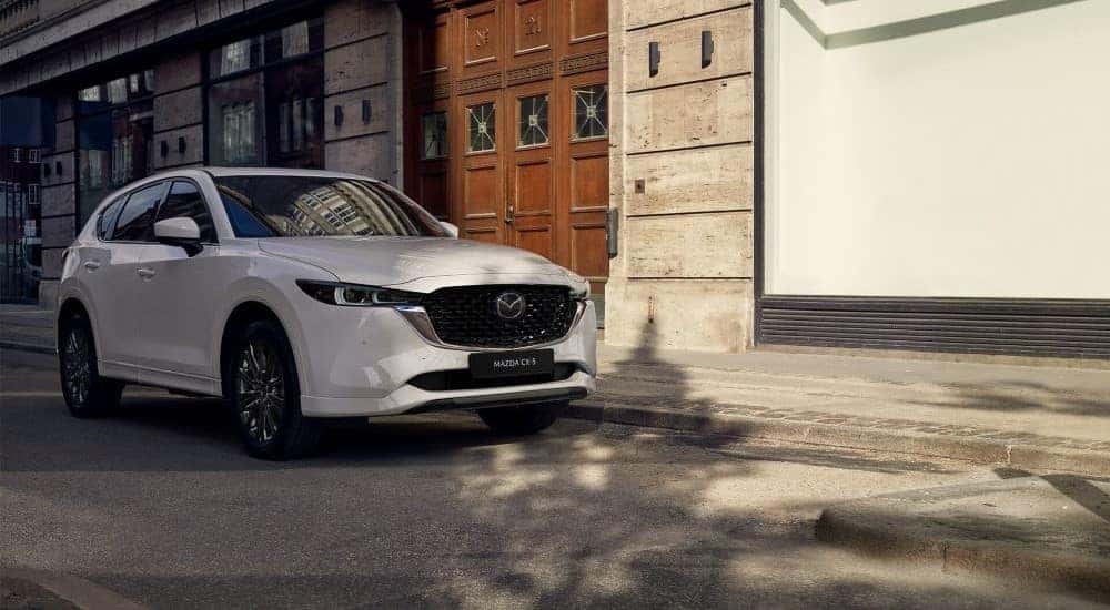 A white 2022 Mazda CX-5 driving by buildings.