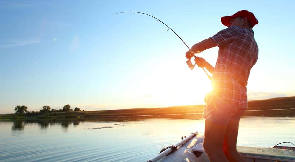 Woman standing on a boat, fishing, with the sun rising behind her