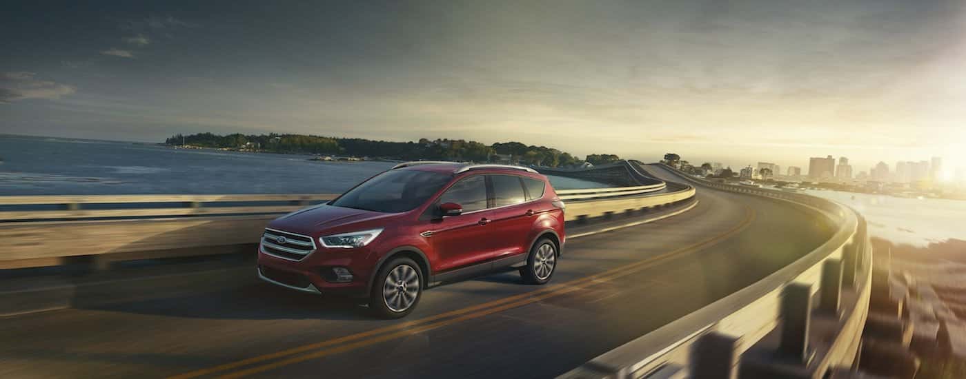 A red 2017 Ford Escape is driving on a bridge over a bay.