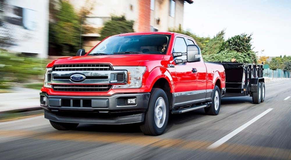 Red Ford F-150 with a trailer hooked on the back driving past houses