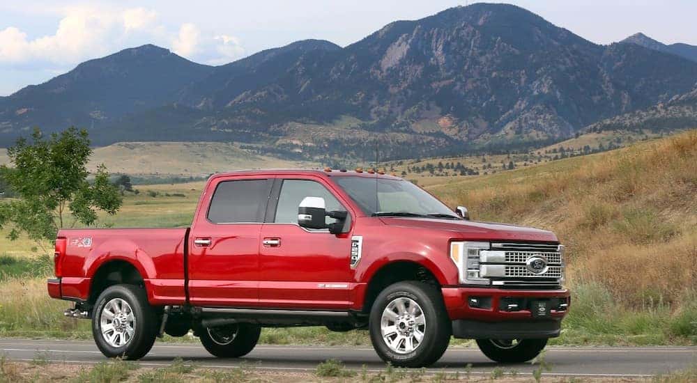 Red 2017 Ford F-250 Super Duty pickup truck parked on a paved road with green fields and dark mountains in the distance