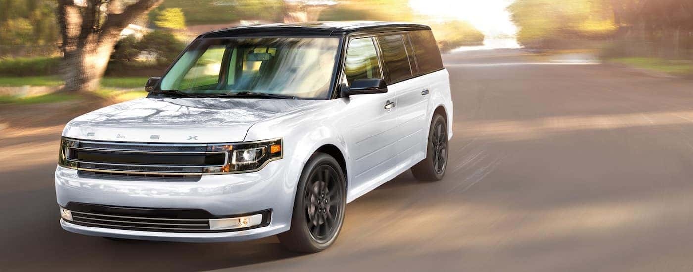 A white 2018 Ford Flex is driving down a sunny street near Albany, NY.