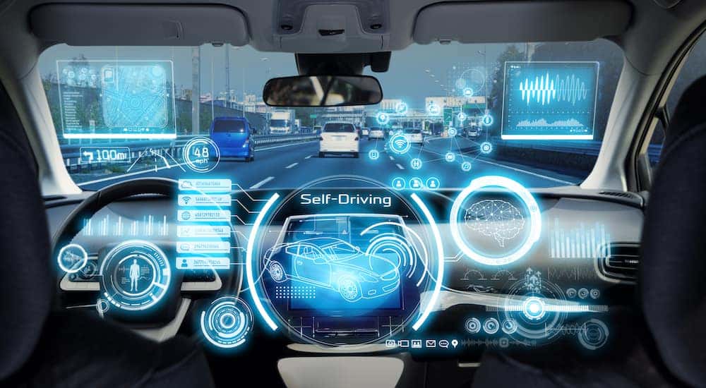 Inside of a vehicle with blue symbols and words floating in the air representing autonomous driving