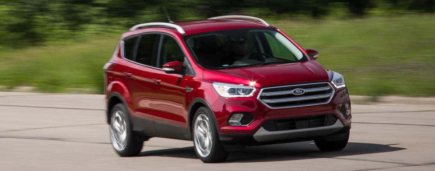 A red 2018 Ford Escape is driving on a grass lined road near Albany, NY.