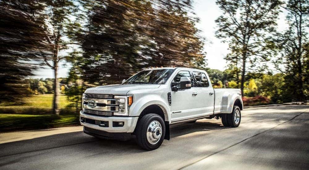 White 2018 Ford F-Series Super Duty truck driving on a paved road past trees and grass
