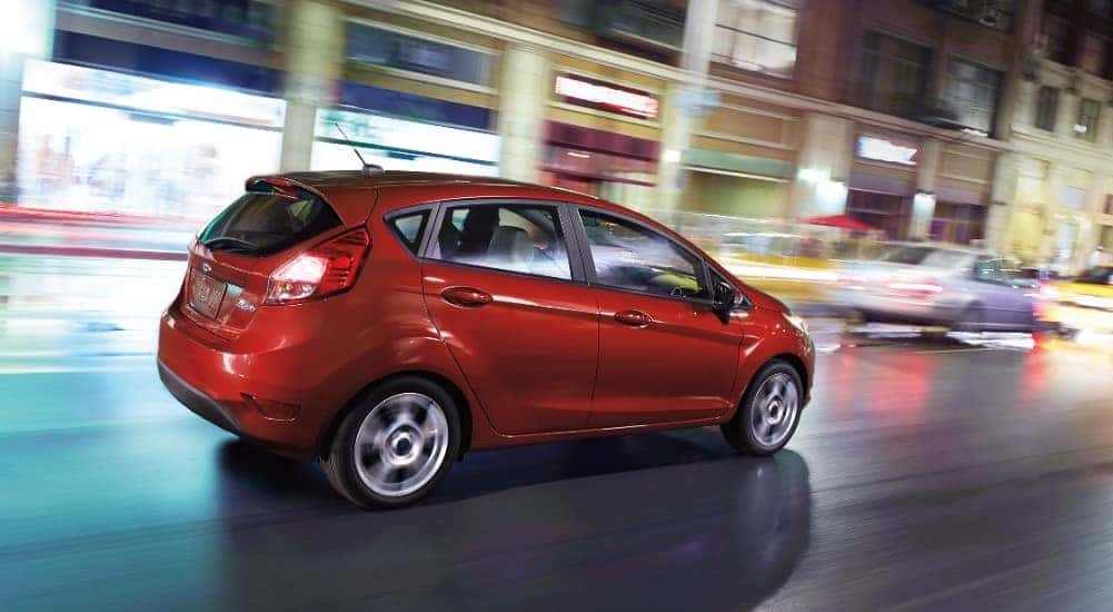Red 2018 Ford Fiesta hatchback driving down a road next to store fronts available at all Ford dealerships.