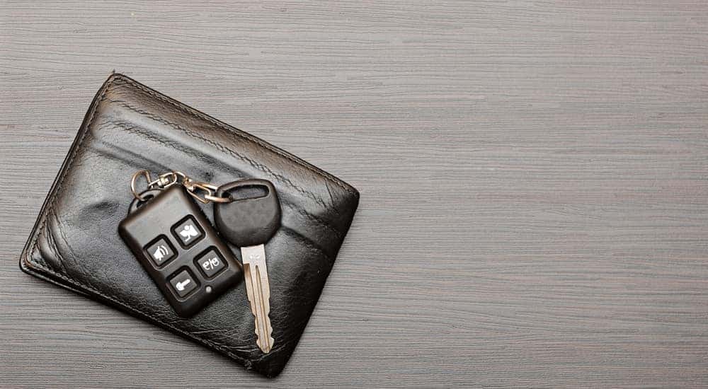 Black wallet with car keys on top of it sitting on a grey wood table