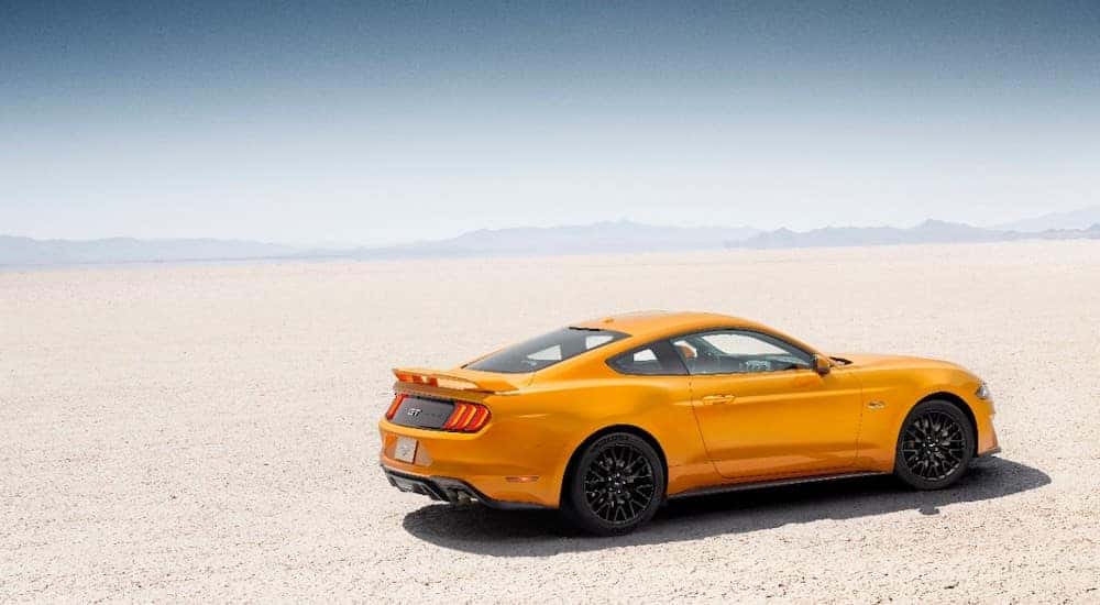 Orange 2018 Ford Mustang parked on flat, light colored ground with mountains in the distance