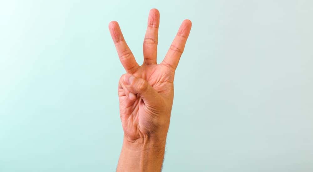 Hand with three fingers up in front of a blue wall