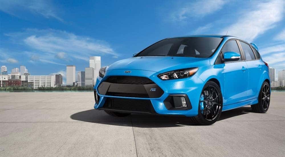 Bright blue 2017 Ford Focus parked on cement with tall buildings in the background