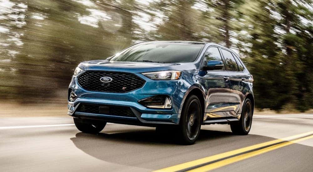 Blue 2019 Ford Edge SUV driving on a blue and yellow paved road past green trees