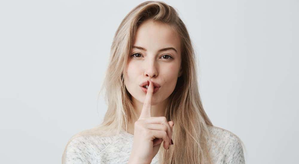 Blonde woman holding her finger up to her lips, shushing after searching used car prices.