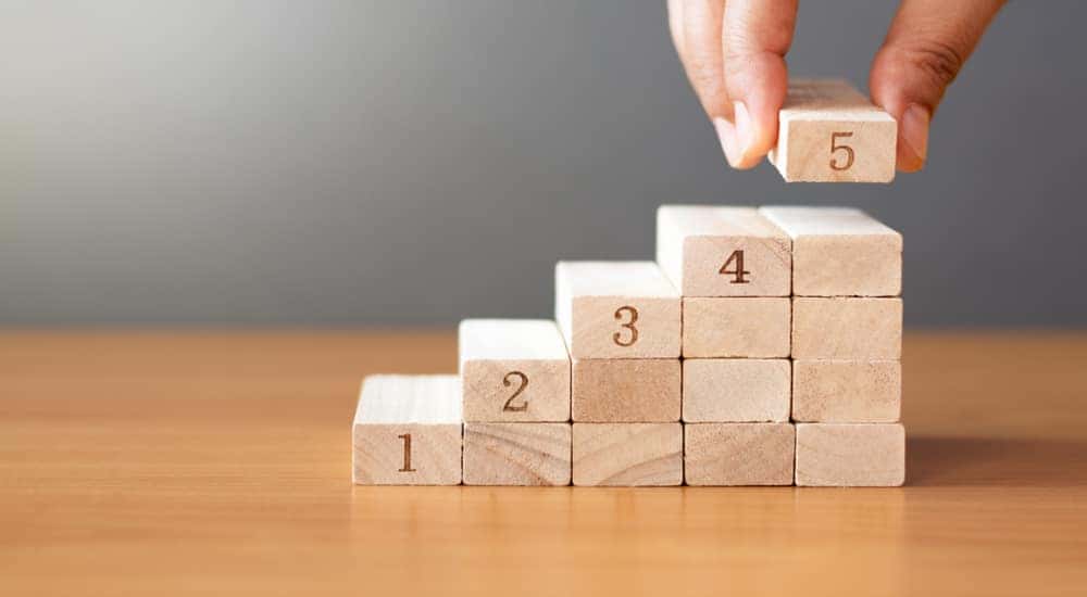 Hand stacking brown blocks numbered 1 to 5 in a stair formation on a brown table after searching for used trucks for sale.