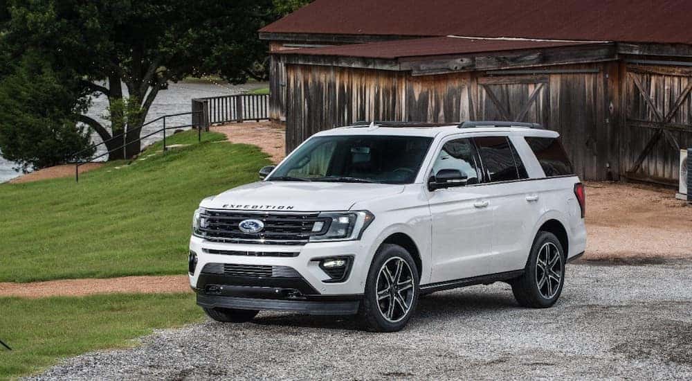 White 2019 Ford Expedition SUV parked in front of a brown building with a pond in the background after the owner searched ''used SUVs for sale''.