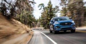 Blue 2019 Ford Edge ST SUV driving around a bend surrounded by trees during the day on a back road