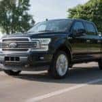 black 2019 Ford F-150 crew cab pick-up truck with chrome grille driving quickly down a road by a body of water