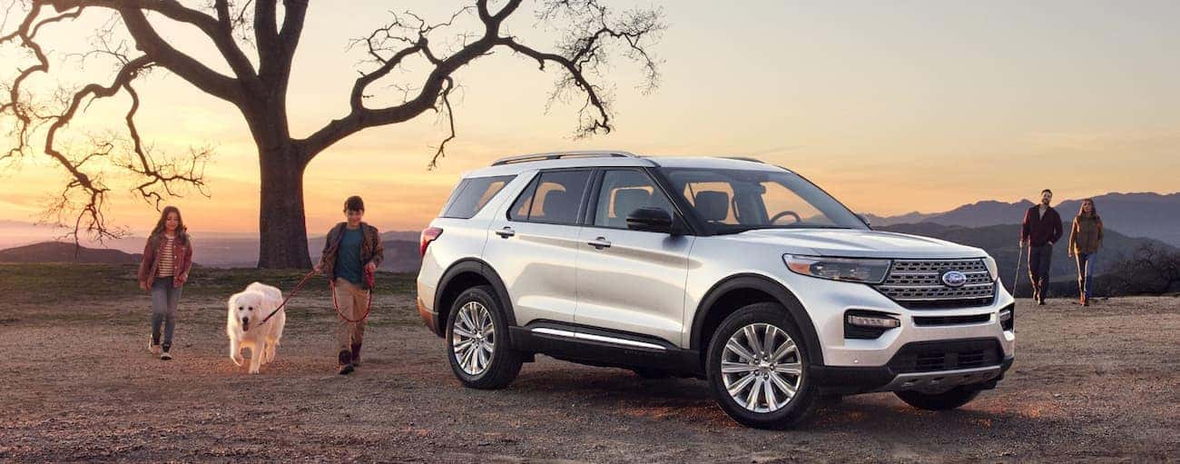 A white 2020 Ford Explorer is parked on a hill near Albany, NY while a family and their dog play around it.
