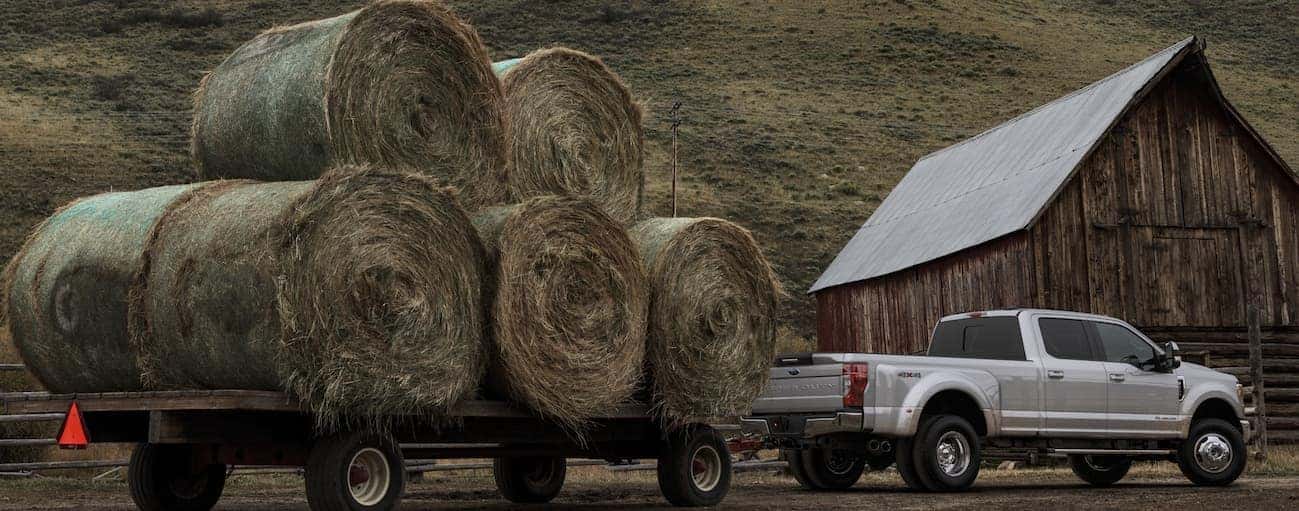 A silver 2020 Ford Super Duty is towing a large trailer with hay bails on it near Albany, NY.