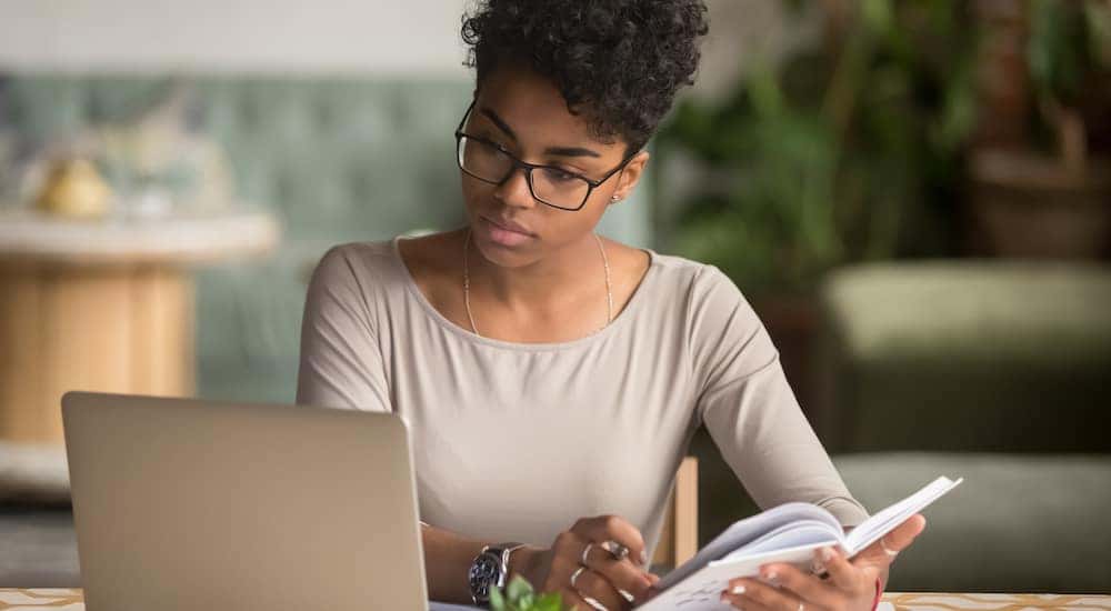 Woman using a silver laptop and holding a white book