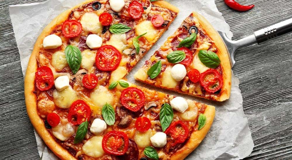 A speciality made pizza, similar to what you could find at a local pizza place in Albany, NY, is shown with cheese, feta, tomato, and more toppings.