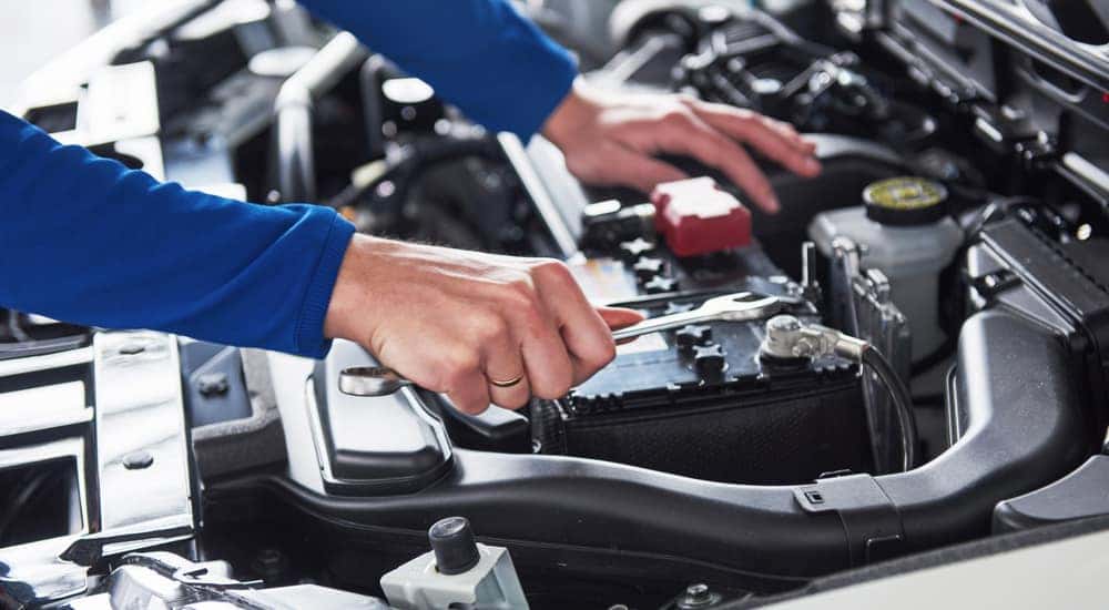 Arms in a blue shirt and hands working with tools under the open hood of a vehicle