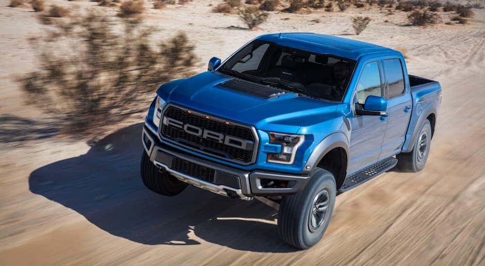 A blue 2018 Ford Raptor is driving down a dirt trail.