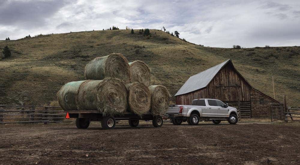 Silver Ford F-350 truck pulling hay on a trailer in front of a barn