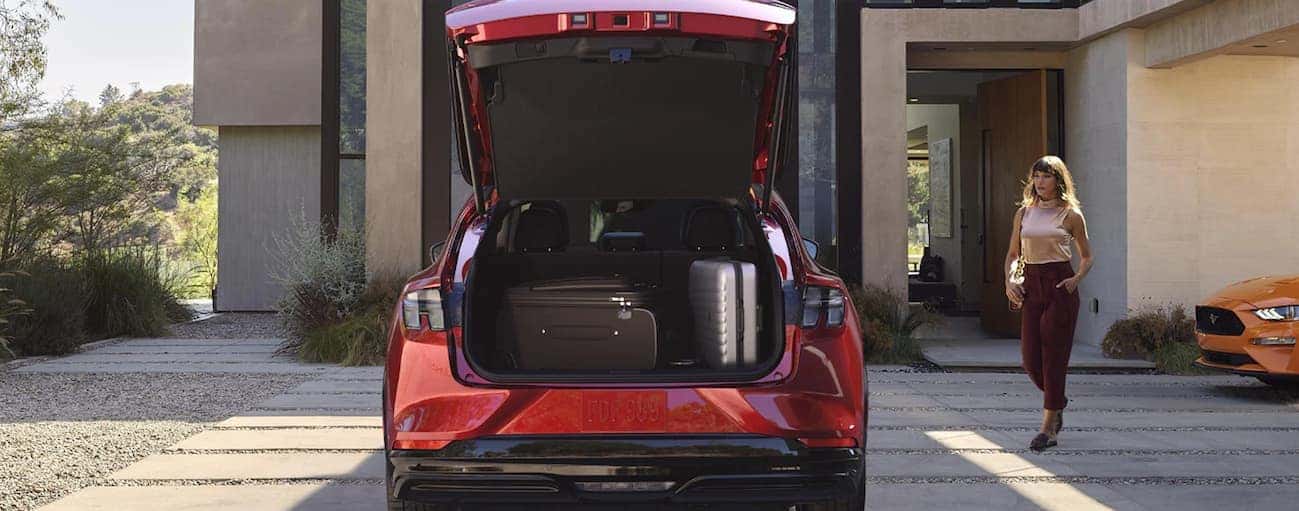A woman is walking to her red 2021 Ford Mustang Mach-E that has the liftgate open with luggage in the trunk.