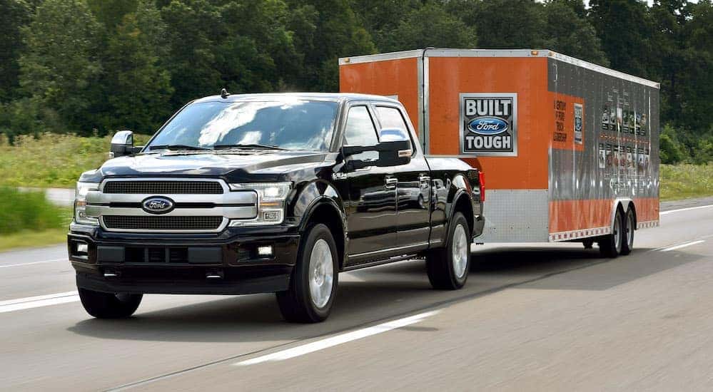 A black 2018 Ford F-150, which is a popular model when searching for "used car dealer near me," is towing a large enclosed trailer near Albany, NY.