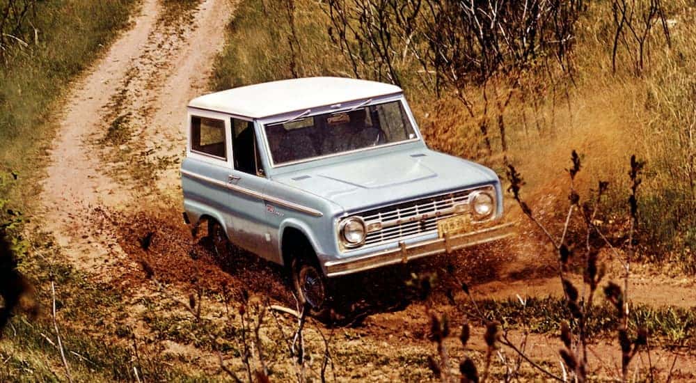 A blue and white 1967 Ford Bronco is off-roading in the mud near Albany, NY.