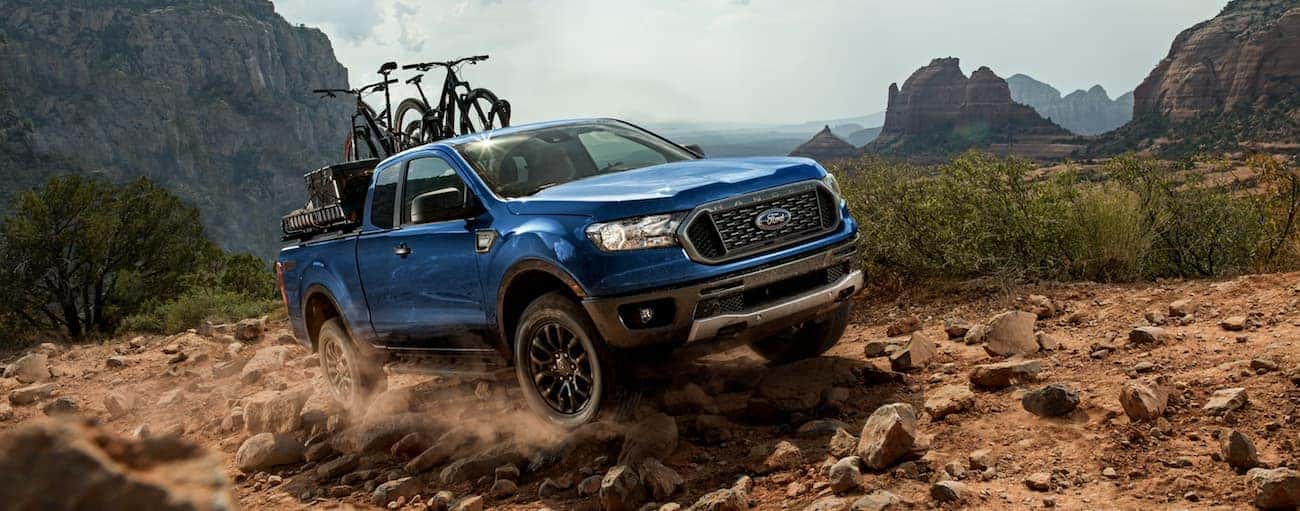 A blue 2020 Ford Ranger with bikes in the bed is off-roading in a mountainous area.