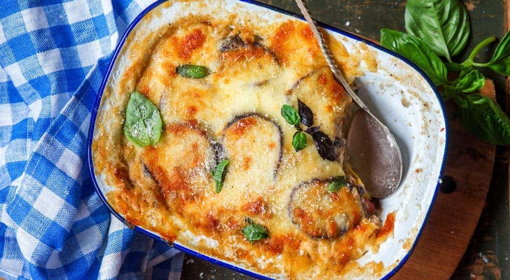 A dish of Moussaka is next to a blue dish towel.