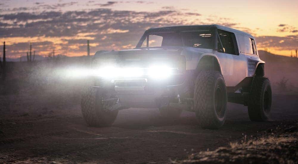 A 2021 Ford Bronco prototype is in the desert at sunset with the headlights shining, which will be popular among Ford SUVs in Albany, NY, after its release.